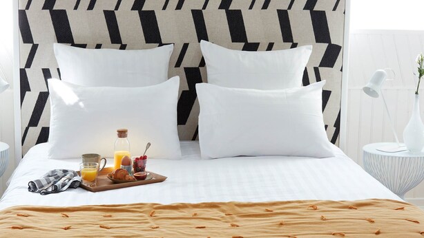 A neatly made bed with a patterned headboard, a tray of breakfast items, and a bedside table with a lamp and vase.