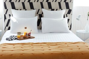 A neatly made bed with a patterned headboard, a tray of breakfast items, and a bedside table with a lamp and vase. - LE 64, Chambre Bois DES Combles (EU)