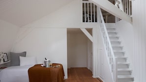 A bedroom with a bed, a nightstand, a table with a drink, and a staircase.