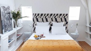 A bedroom with a bed, wooden floor, white walls, a chevron-patterned headboard, and a window.