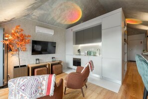 Una sala de estar moderna con televisor, asientos, chimenea y una zona de cocina con armarios y electrodomésticos.