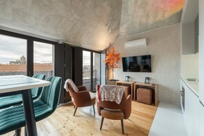 Un espacio moderno de estar con zona de comedor, dos sillones, una mesa, un televisor y una planta.