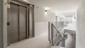 Un edificio moderno con tres ascensores, una escalera con barandillas de metal y un interior limpio y blanco.