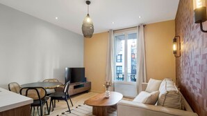 A modern living room with a sofa, dining table, chairs, a TV, and a large window with curtains. - 11.Appart 4Pers#1 Bedroom #Père Lachaise #Nation (Paris)