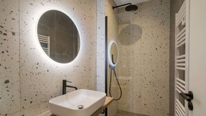 Ein modernes Badezimmer mit freistehender Waschtisch, einem runden Spiegel und einer Duschkabine.