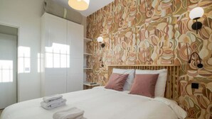 Ein Hotelzimmer mit einem großen Bett, einem Kleiderschrank, einem Nachttisch und einer Wand mit Muster.