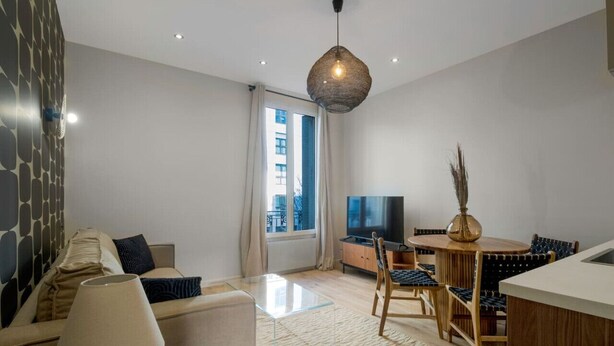 Ein modernes Wohnzimmer mit einer Couch, einem Couchtisch, einem Fernseher und einem Essbereich mit Stühlen und einem Tisch.