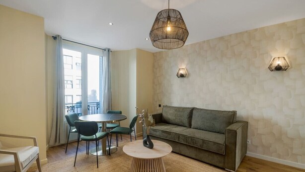 Ein modernes Wohnzimmer mit einem runden Couchtisch, einer grauen Couch und einem Essbereich mit rundem Tisch und Stühlen.