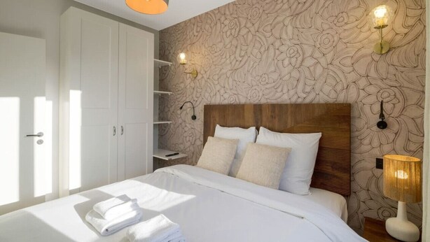 Ein Schlafzimmer mit einem großen Bett, weißen Leinentüchern, einem Holzkopfende und Wandtapete mit Muster.