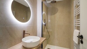 Ein modernes Badezimmer mit einem runden Spiegel, einem weißen Waschbecken und einer Duschkabine.