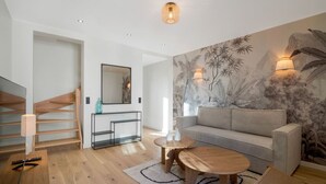 Un salon moderne avec un escalier, un canapé, deux tables basses et une fresque murale.
