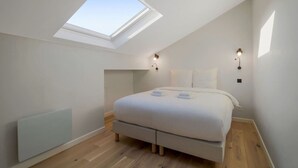 Une chambre avec un puits de lumière, un lit, deux lampes fixées au mur et un radiateur.