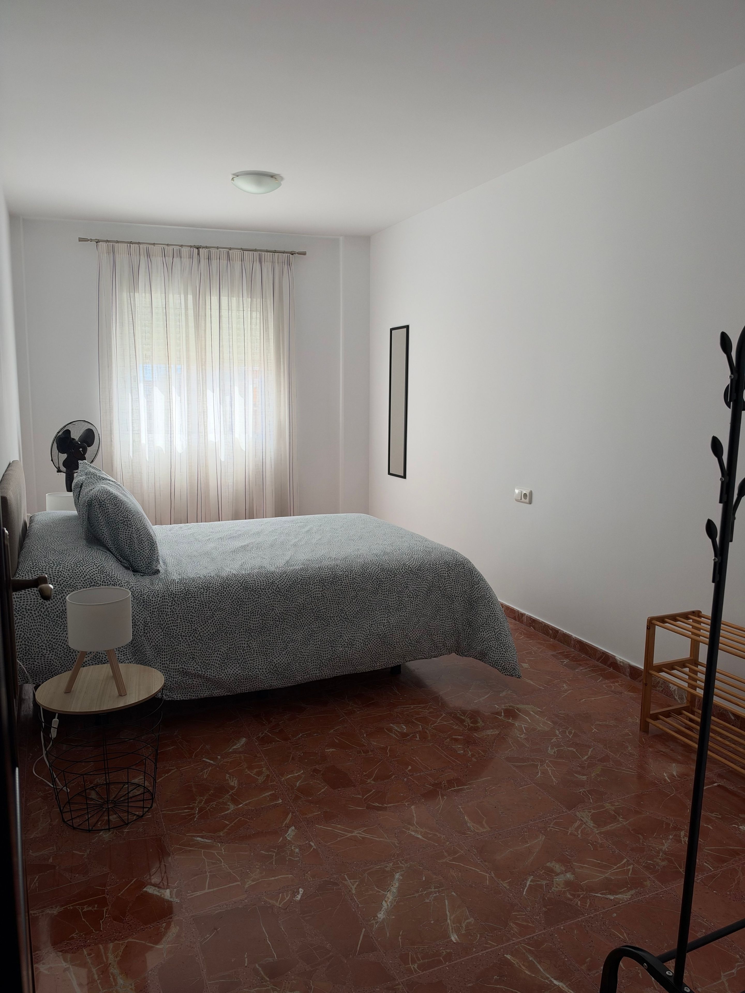 Un dormitorio con cama, mesita de noche, lámpara, ventana con cortinas y radiador.