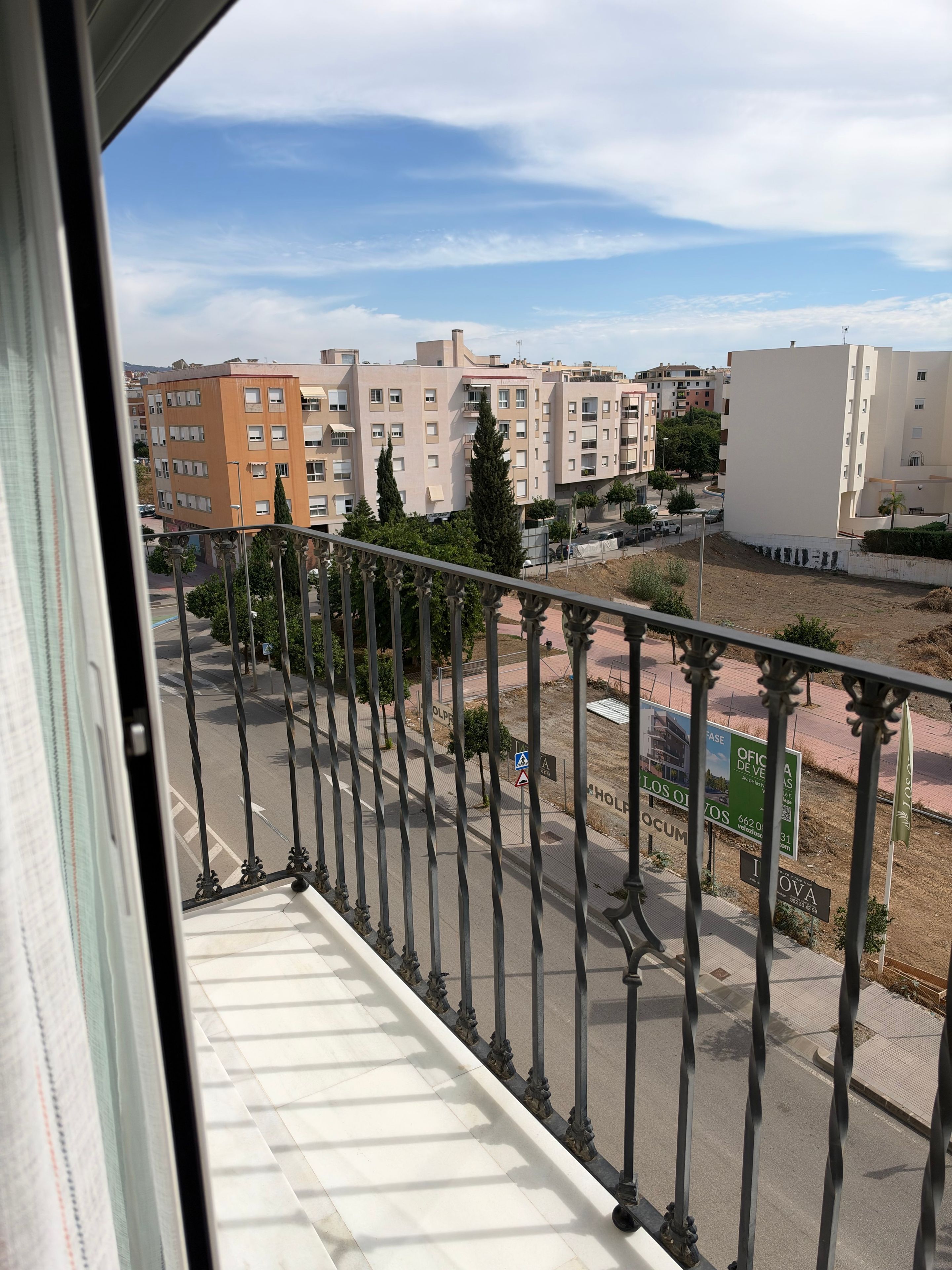 Un balcón con vista a un paisaje urbano, que incluye edificios y una carretera.