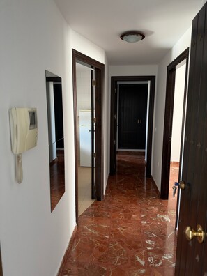 A hallway with a telephone on the wall, a marble floor, and doors leading to other rooms.