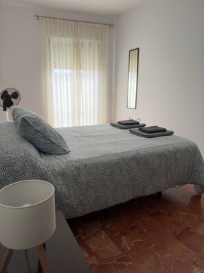 Una camera da letto con un letto, un comodino, una lampada, una ventola e una finestra con tende.