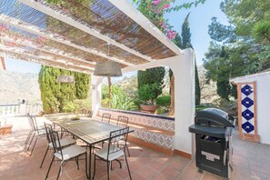 An outdoor patio with a table and chairs, a grill, and a pergola with a woven roof. - Villa 'Casa Chatsee' with Mountain View, Wi-Fi and Air Conditioning (Torrox)