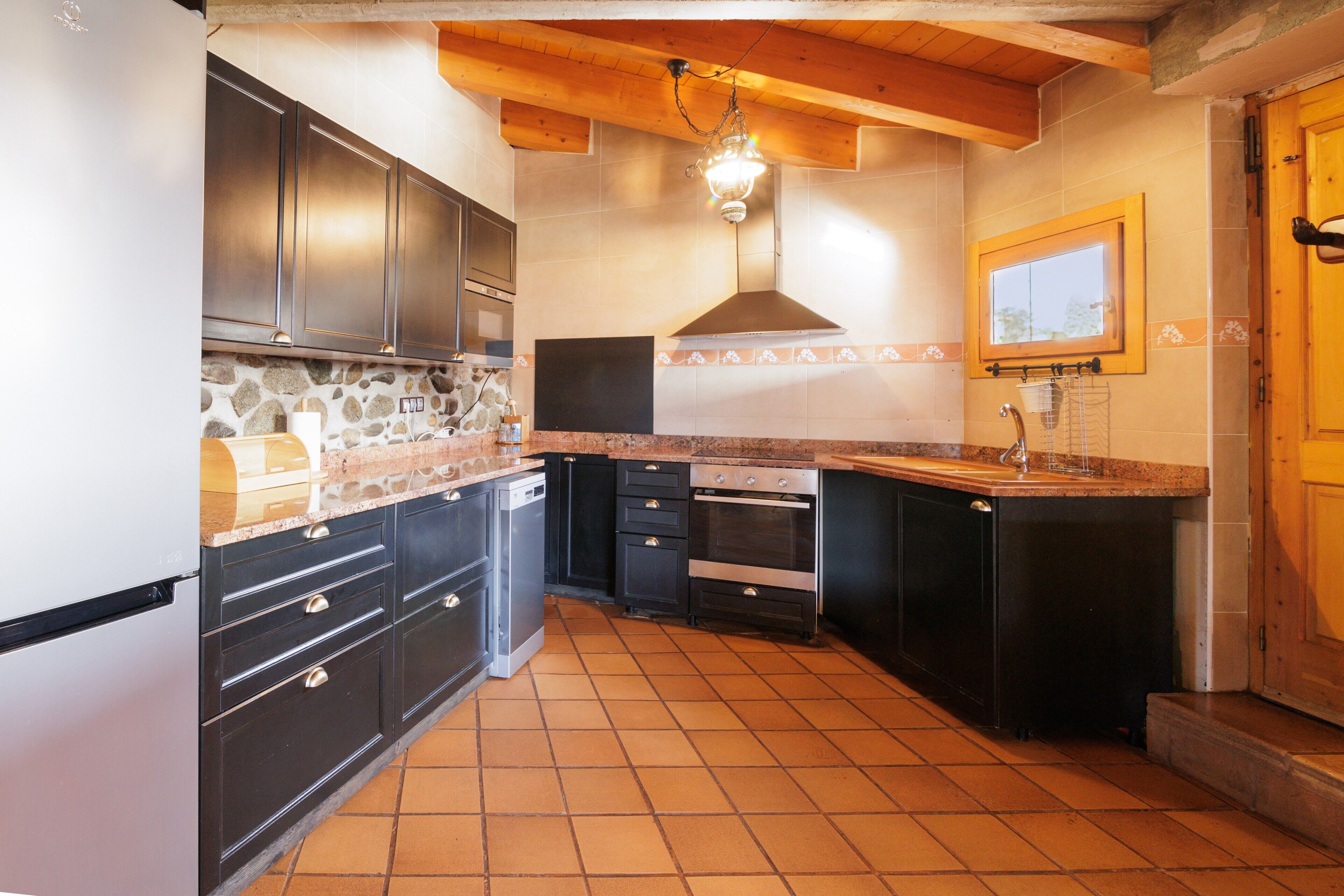 A kitchen with dark cabinets, a stone backsplash, and a tiled floor.