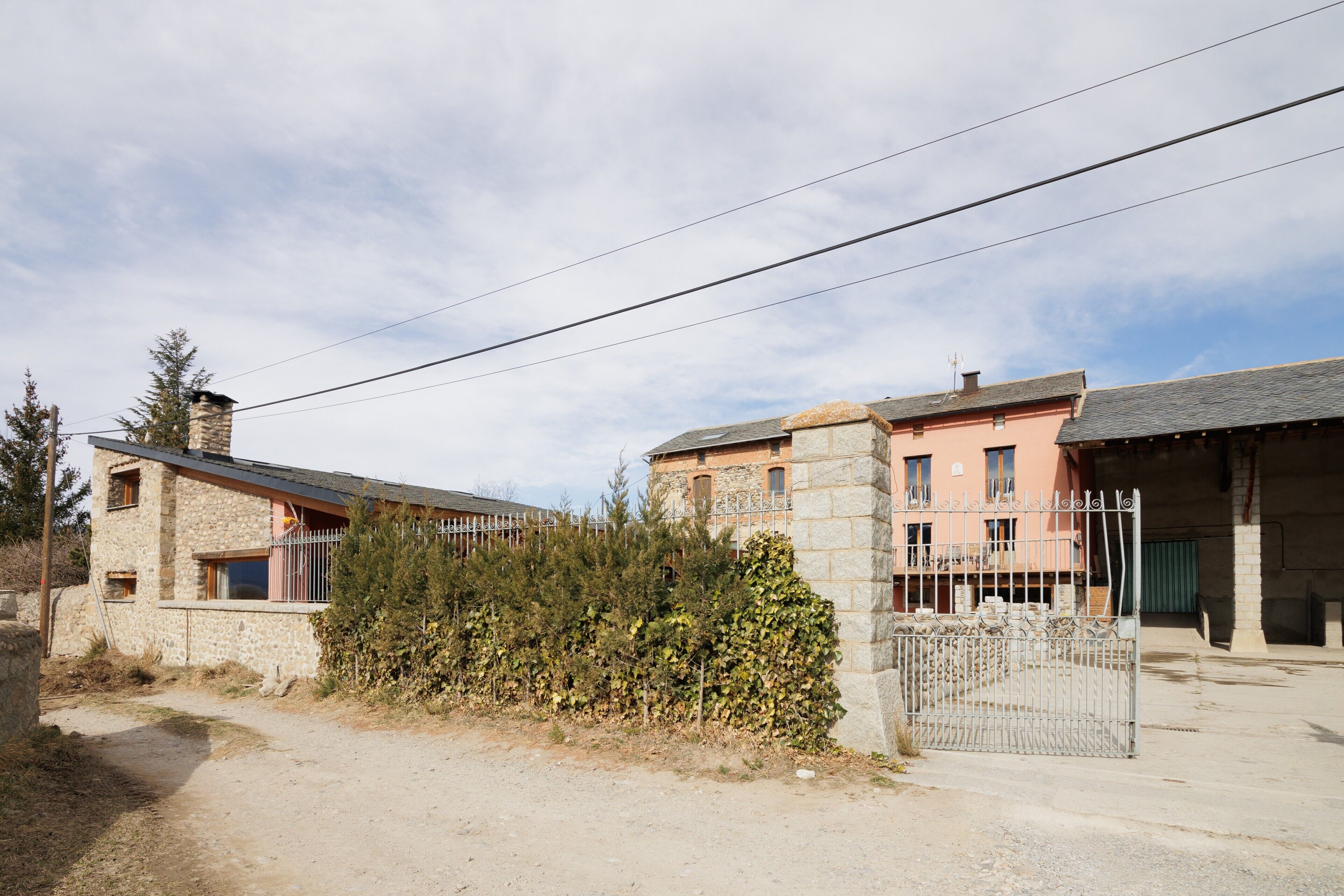 A rustic stone building with a metal gate, a dirt path, and a clear sky.