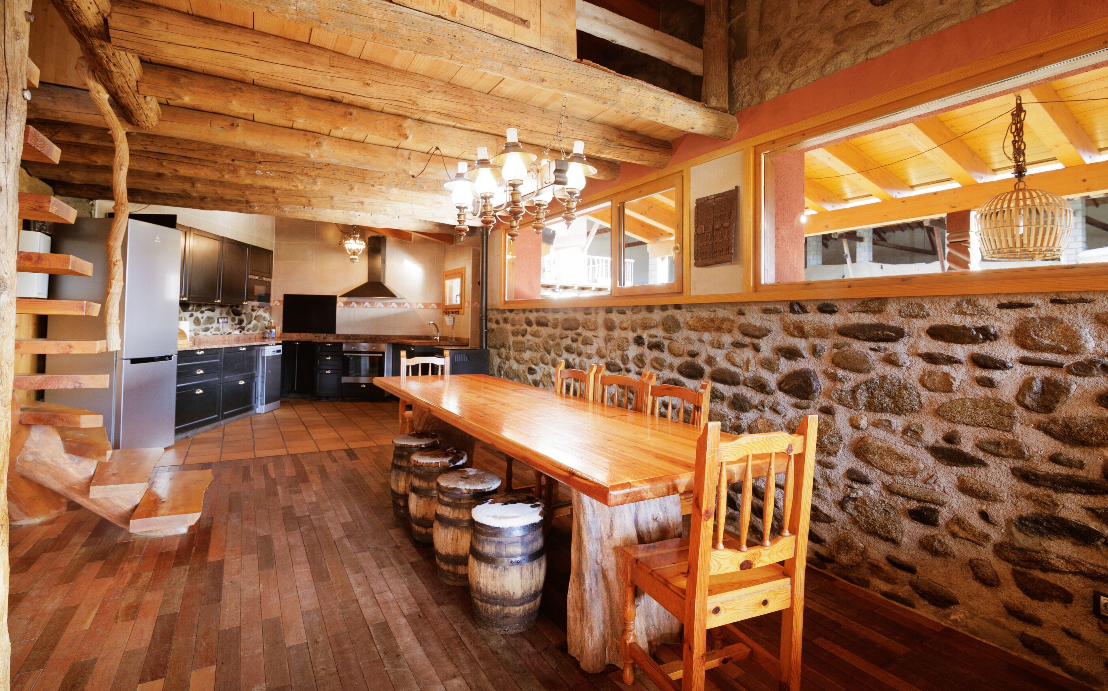 A rustic kitchen with wooden beams, a stone wall, and a wooden dining table with chairs.