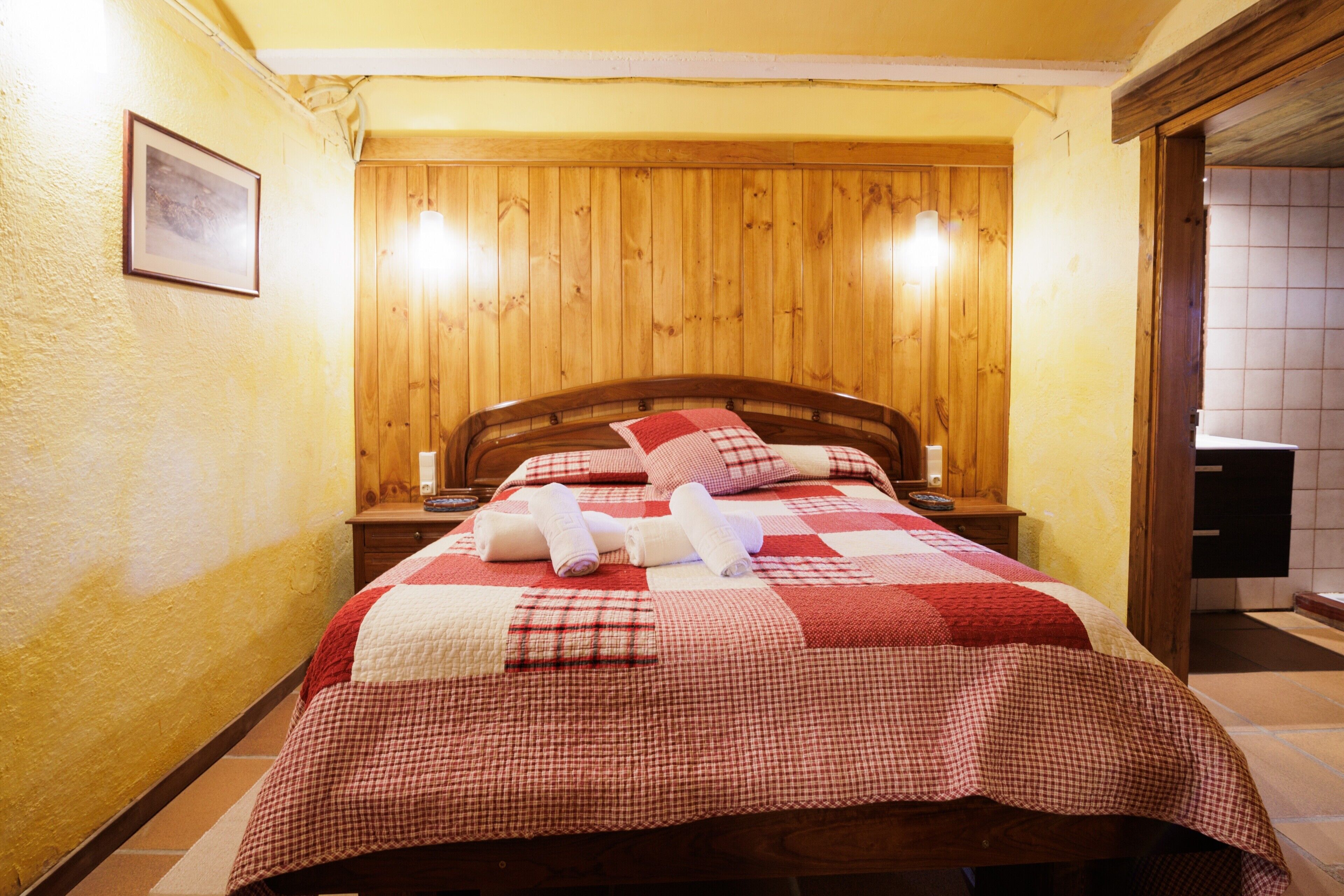 Una cama con colcha a cuadros, cabecera de madera y dos mesitas de noche con lámparas.