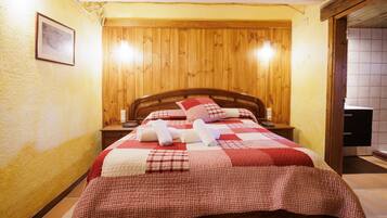 Una cama con colcha a cuadros, cabecera de madera y dos mesitas de noche con lámparas.