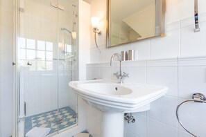 Ein Badezimmer mit einer Duschkabine aus Glas, einem weißen Waschbecken mit Chromarmatur und einem Spiegel darüber.