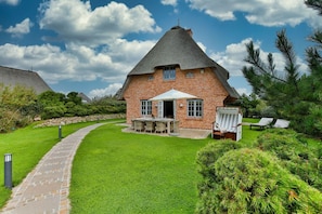 A brick house with a thatched roof, a patio with outdoor furniture, and a well-maintained lawn. - Klenterhüüs - Klenterhüüs - Hochwertig und Exklusiv Ausgestattetes Ferienobjekt (Sylt-Ost)