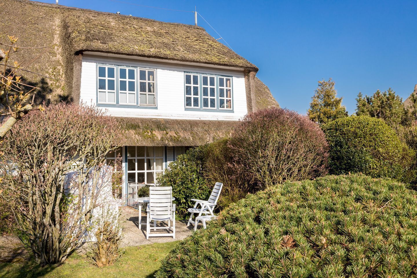 A traditional house with a thatched roof, a white exterior, and a small patio with two white chairs.