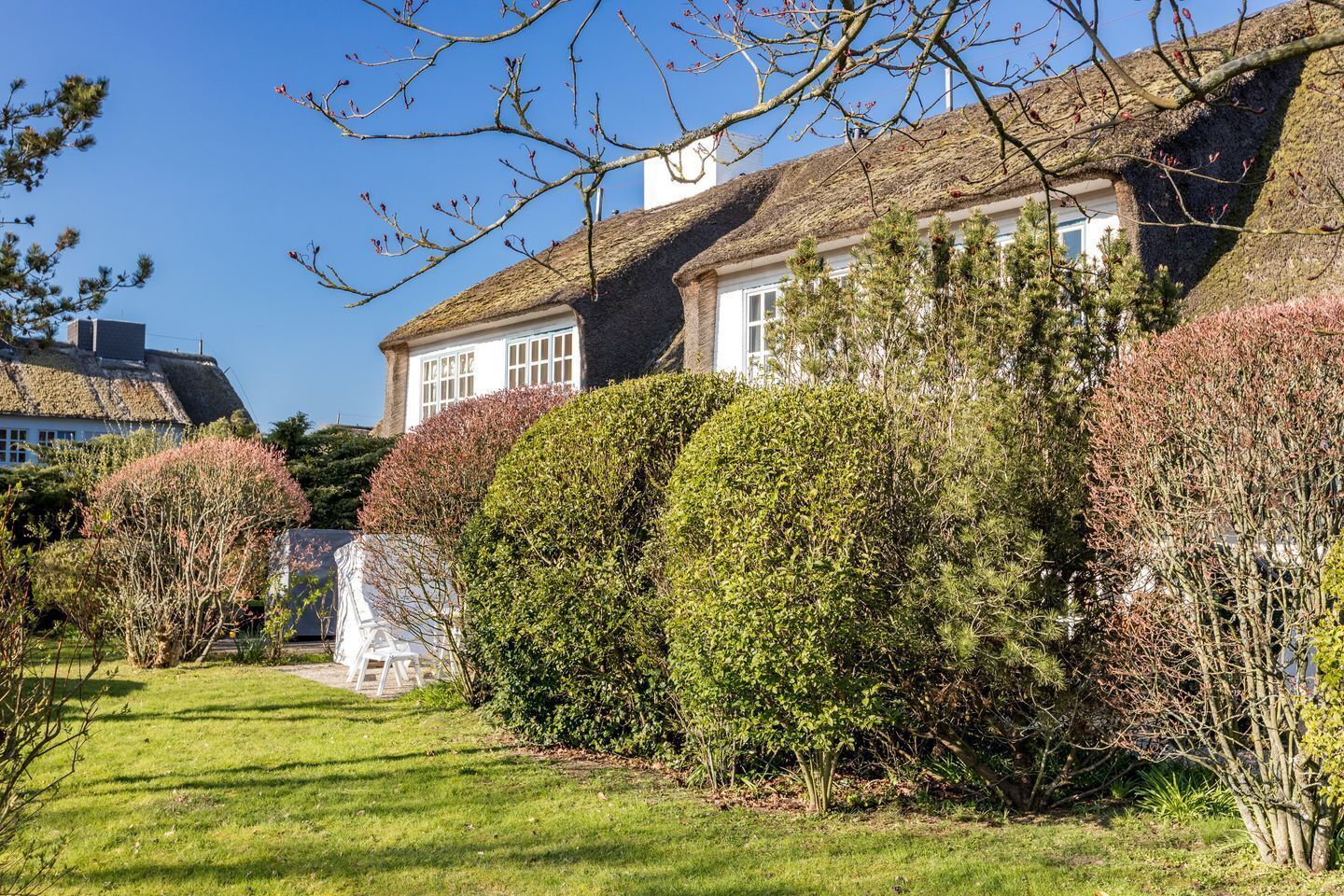 A traditional house with a thatched roof, surrounded by well-maintained hedges and a lawn.