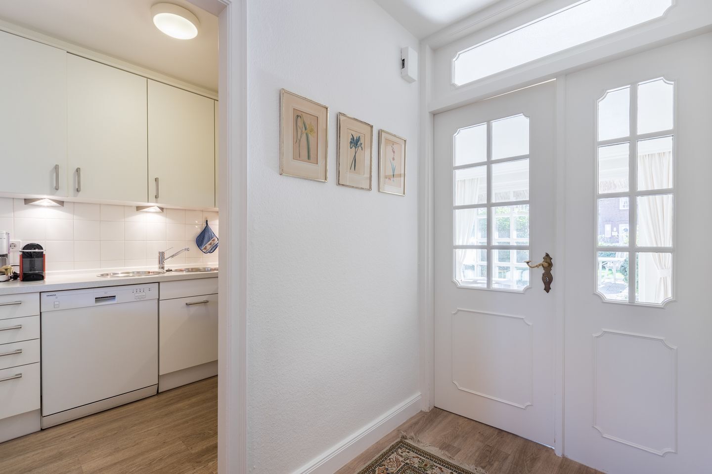 A kitchen with white cabinets, a sink, and a coffee maker. There are three framed pictures on the wall.