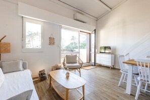 Una habitación con cama, una mesa de comedor con sillas, un televisor y una ventana con vista a árboles.