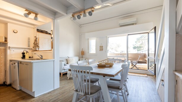 Een moderne keuken met witte kasten, een ingebouwde vaatwasser en een eethoek met een houten tafel en witte stoelen.