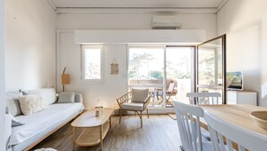 Een moderne woonkamer met een bank, eettafel, stoelen en een groot raam.