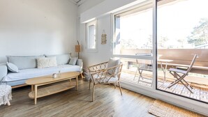 Een moderne woonkamer met een bank, salontafel, rieten stoel en grote ramen.