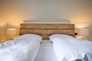 A double bed with a padded headboard, two bedside lamps, and white bedding.
