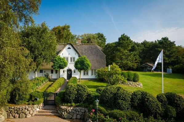 A white house with a thatched roof, surrounded by well-maintained gardens and a flagpole.
