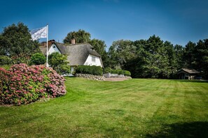 A traditional thatched-roof house with a stone wall and a flagpole.