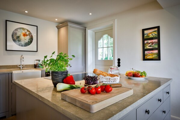 A modern kitchen with a marble countertop, a sink, a potted plant, fresh vegetables, and a window with natural light.