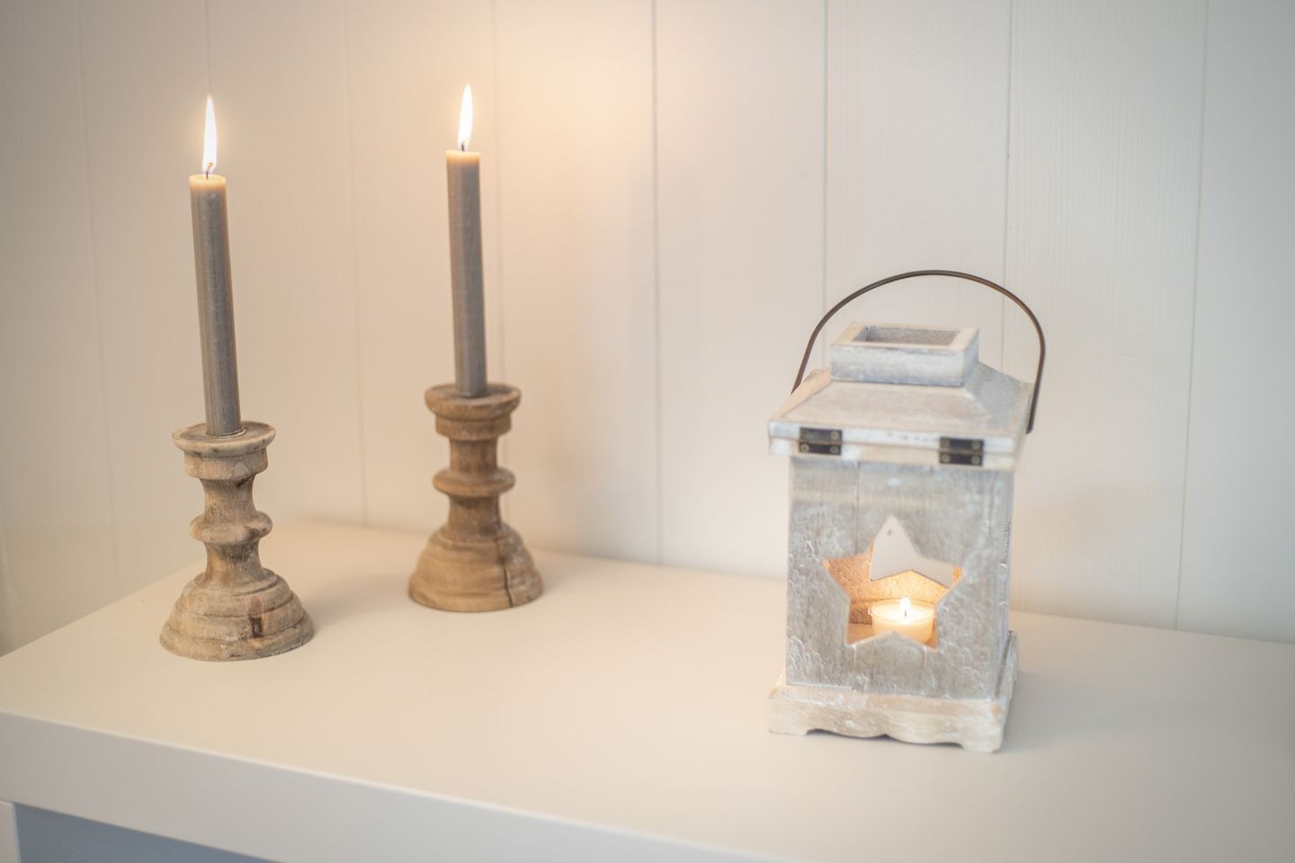 Two candles on a white shelf and a lantern with a star-shaped window.