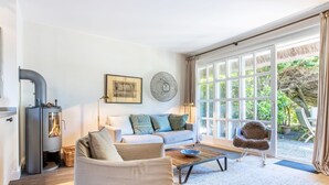 Un salon moderne comprenant un canapé, une table basse, un fauteuil, une cheminée et une grande fenêtre donnant sur un paysage verdoyant.