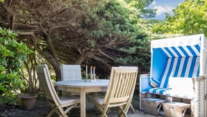 Une table ronde en bois, accompagnée de quatre chaises, d’une plante en pot et d’une structure rayée bleue et blanche.