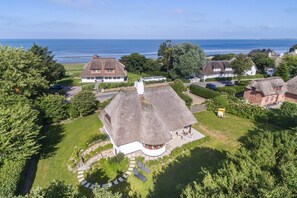Ein Küstenanwesen mit reetgedeckten Hütten, einer Rundterrasse und Blick auf das Meer.