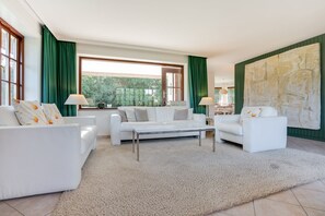 Ein modernes Wohnzimmer mit weißen Möbeln, einem großen abstrakten Gemälde und grünen Vorhängen.