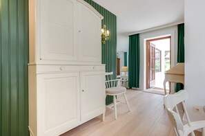 Ein Zimmer mit einem weißen Kleiderschrank, einem Klavier, einem Sessel und einem Tisch.