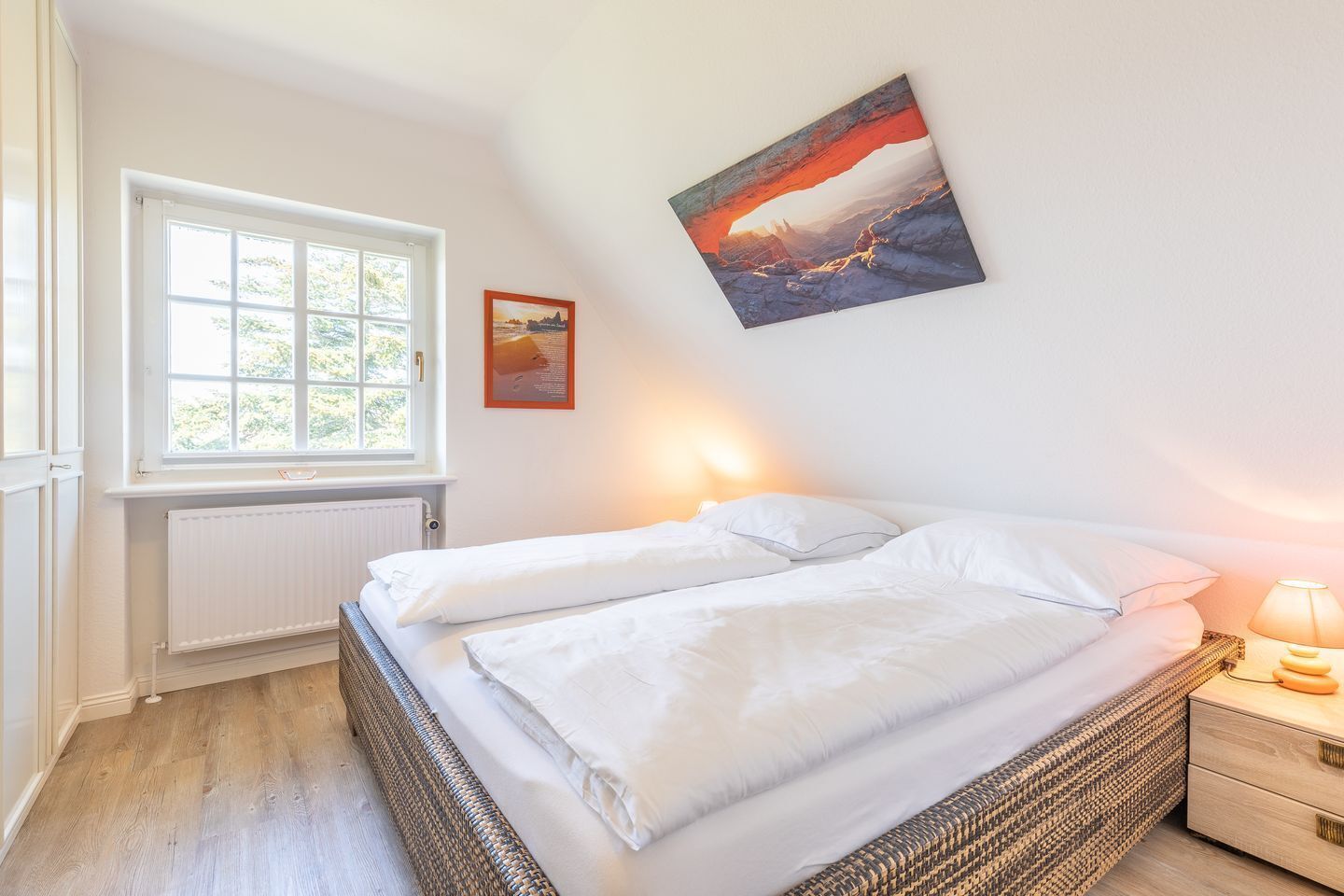 Un dormitorio con cama, ventana, radiador, lámpara de pared y un cuadro.