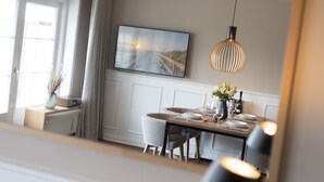 Un comedor con una mesa dispuesta para cuatro personas, un televisor montado en la pared y una lámpara colgante sobre la mesa.