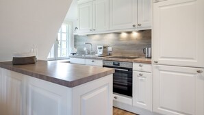 A modern kitchen with white cabinetry, a wooden countertop, stainless steel appliances, and a built-in oven. - Sharky Bay - Die Reetgedeckte, Gepflegte Anlage Liegt auf Einem ca. 2000 m² Großem Grundstück (Sylt-Ost)