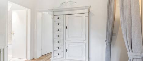 Un armario blanco con varios cajones y puertas, piso de madera y una puerta que da a otra habitación.