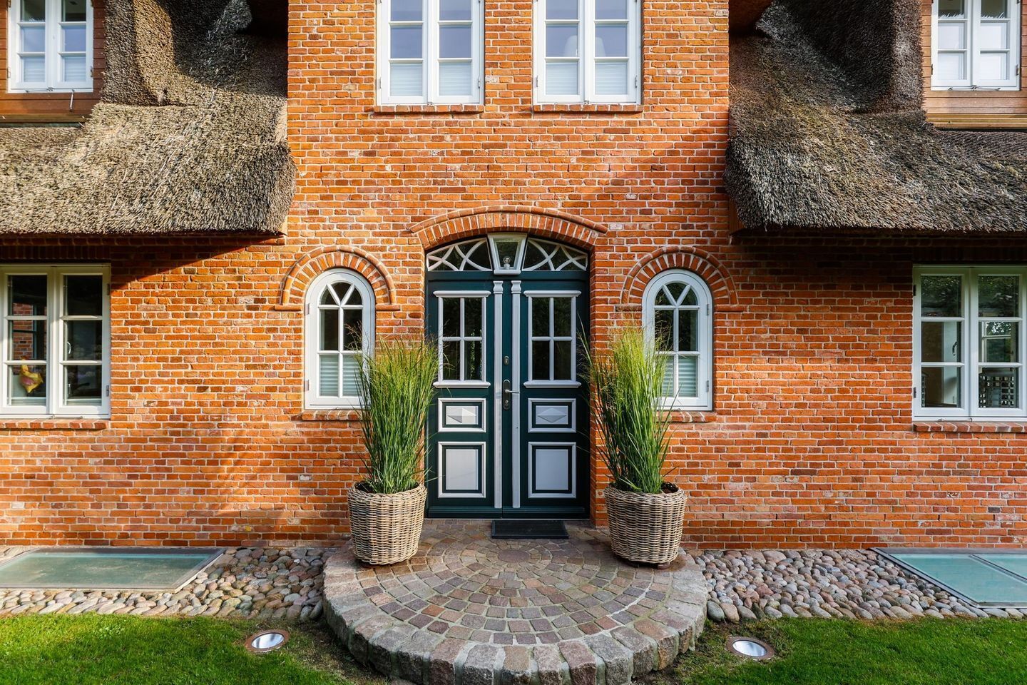A brick building with a central double door, two potted plants, and a stone pathway leading to the entrance.